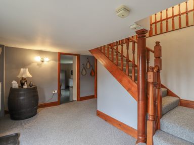 A hallway with carpeted stairs and wooden banister and a black barrel serving as table with a lamp and decor at High Shaftoe in Ponteland