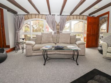 A living room with a sofa pillows glass coffee table and exposed wooden beams at High Shaftoe in Ponteland