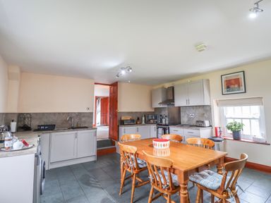 A kitchen with a wooden dining table and chairs a window with a plant kitchen cabinets and appliances at High Shaftoe in Ponteland