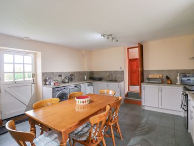 A kitchen with wooden dining table and chairs near a door and cabinets at High Shaftoe in Ponteland