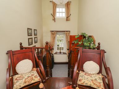 A staircase landing with two wooden chairs with cushions a window with curtains and framed pictures on the wall at High Shaftoe in Ponteland