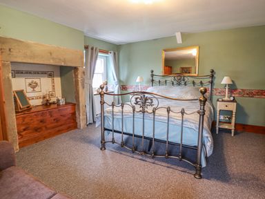 A bedroom with an iron bed frame a wooden chest under a fireplace and bedside tables with lamps at High Shaftoe in Ponteland
