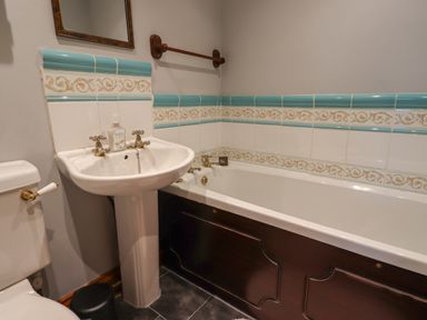 A bathroom with a pedestal sink toilet and bathtub with decorative tiles at High Shaftoe in Ponteland