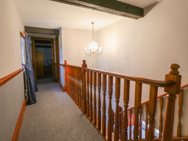 A hallway with wooden railing and carpeted floor with a chandelier hanging from the ceiling at High Shaftoe in Ponteland