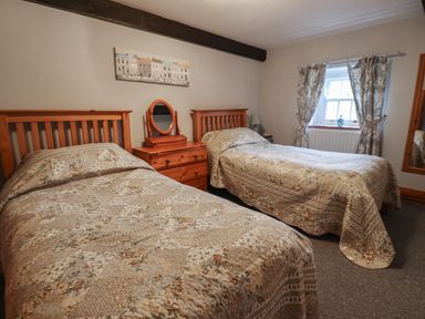 A bedroom with two single beds a wooden dresser between the beds and a window with curtains at High Shaftoe in Ponteland