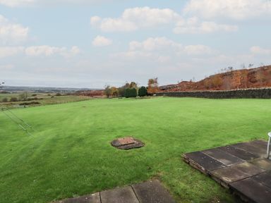 A large green lawn with some trees and bushes near a stone wall in a rural setting at High Shaftoe in Ponteland