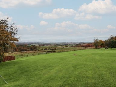 A large green lawn with trees and fields in the distance under a cloudy blue sky at High Shaftoe in Ponteland