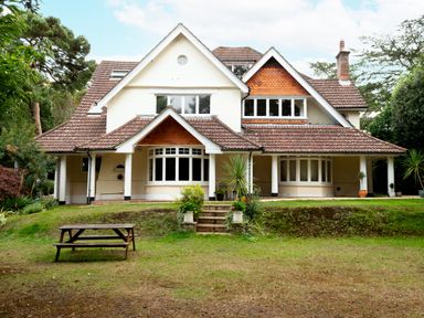 A large house with a tiled roof and covered porch on a grassy lawn with a picnic table