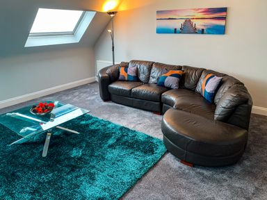 A living room with a black leather sectional sofa with cushions a glass coffee table and a skylight window at The Gables Penthouse in Bournemouth