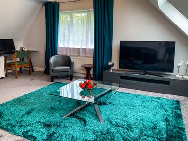 A living room with a glass coffee table on a teal rug and a television on a console at The Gables Penthouse in Bournemouth