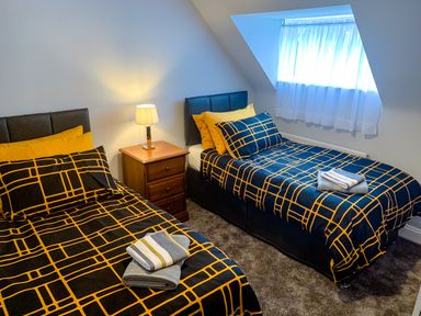 A bedroom with two single beds with patterned bedding and a nightstand with a lamp at The Gables Penthouse in Bournemouth