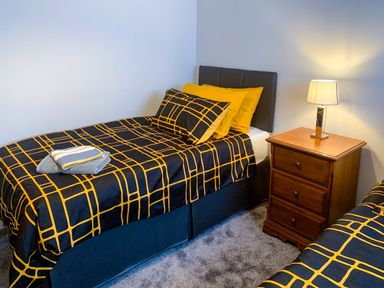 A bedroom with two single beds with patterned bedding and a wooden nightstand with a lamp between them at The Gables Penthouse in Bournemouth