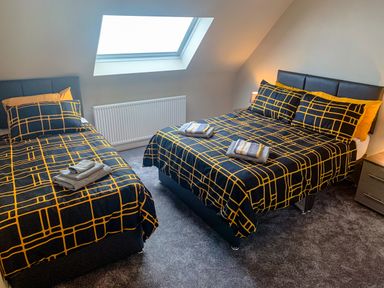 A bedroom with two beds covered in black and yellow checkered bedding under a skylight window at The Gables Penthouse in Bournemouth