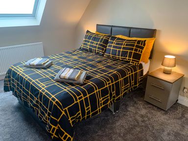 A bedroom with a double bed with patterned bedding and two towels on it next to a nightstand with a lamp at The Gables Penthouse in Bournemouth