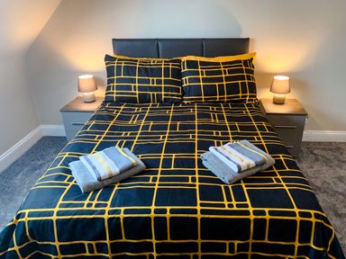 A bedroom with a bed with patterned bedding and two bedside tables with lamps at The Gables Penthouse in Bournemouth