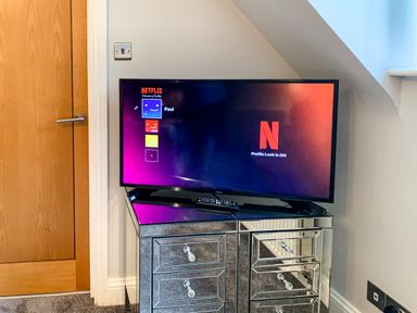 A television displaying the Netflix profile selection screen on a mirrored cabinet next to a wooden door at The Gables Penthouse in Bournemouth