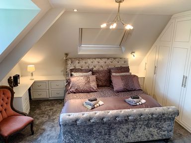 A bedroom with a bed with pillows and folded towels bedside tables built in wardrobes a red chair and a lamp at The Gables Penthouse in Bournemouth