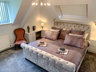 A bedroom with a bed with multiple pillows bedside tables and a chair at The Gables Penthouse in Bournemouth