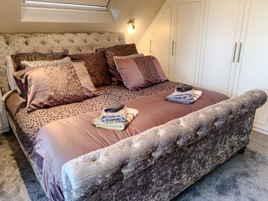 A bedroom with a large bed with pillows and folded towels on the bed near a window and white built-in wardrobes at The Gables Penthouse in Bournemouth