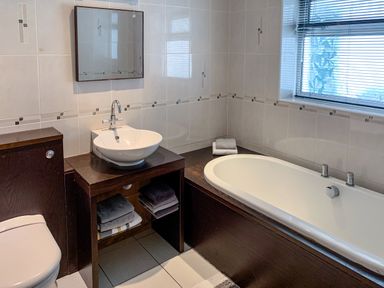 A bathroom with a toilet a sink with towels and a bathtub under a window at The Gables Penthouse in Bournemouth