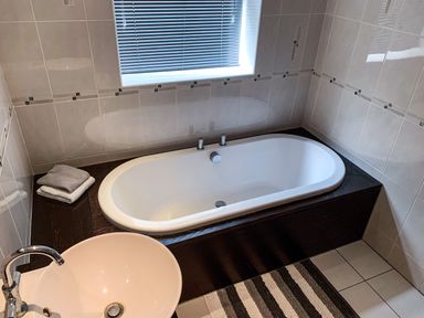 A bathroom with a bathtub sink striped rug and folded towels at The Gables Penthouse in Bournemouth