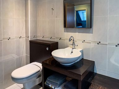 A bathroom with a toilet and a sink with a faucet and mirror above at The Gables Penthouse in Bournemouth