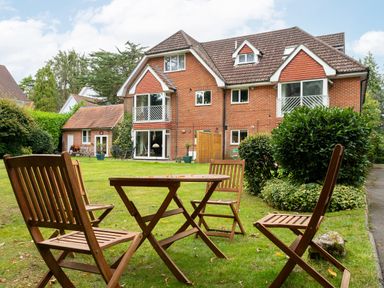 A garden with wooden chairs and a table in front of a brick house with balconies at The Gables Penthouse in Bournemouth