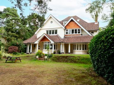 A large two story house with a porch and tiled roof surrounded by trees and a lawn with a picnic table at The Gables Penthouse in Bournemouth