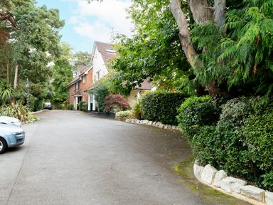 A driveway with parked cars and a house surrounded by trees and bushes at The Gables Penthouse in Bournemouth