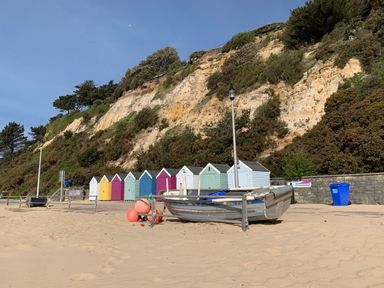 A sandy beach with a small boat and colorful beach huts at the base of a cliff at The Gables Penthouse in Bournemouth