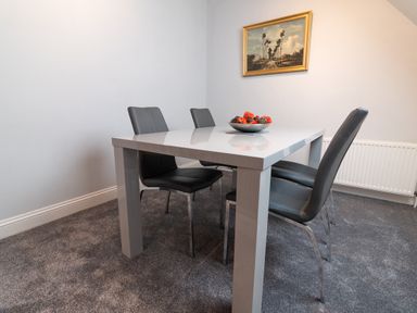 A dining area with a white table and four gray chairs with a bowl of decorative items on the table and a painting on the wall at The Gables Penthouse in Bournemouth