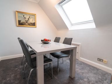 A dining area with a white table and four black chairs under a skylight window at The Gables Penthouse in Bournemouth