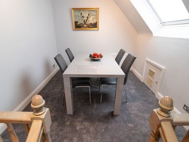 A dining area with a white table and four gray chairs a bowl with decorations on the table a framed picture on the wall and a skylight window at The Gables Penthouse in Bournemouth