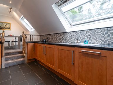 A kitchen with wooden cabinets a black countertop and mosaic tile backsplash near a dining area at The Gables Penthouse in Bournemouth