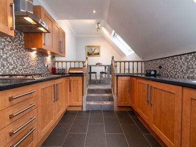 A kitchen with wooden cabinets and black countertops leading to a dining area with a table and chairs at The Gables Penthouse in Bournemouth