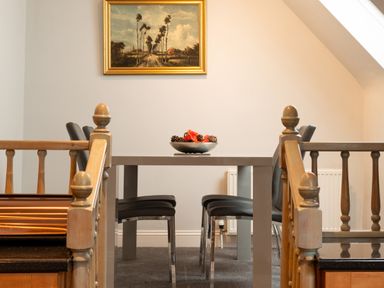 A dining table with four chairs and a bowl with pine cones and flowers on the table under a framed painting at The Gables Penthouse in Bournemouth