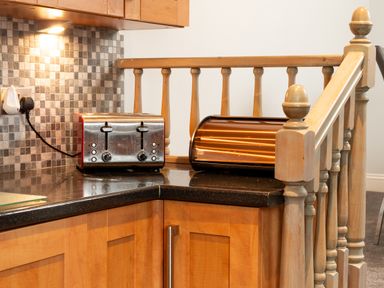 A kitchen corner with a toaster and a bread box on a black countertop with wooden cabinets and a tiled backsplash at The Gables Penthouse in Bournemouth