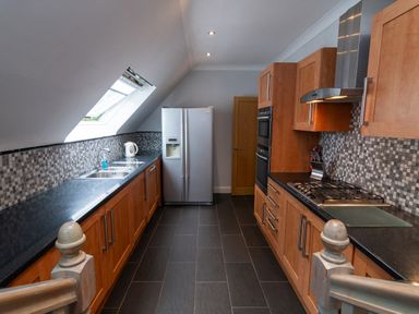A kitchen with wooden cabinets a double door refrigerator a gas stove and a slanted skylight window at The Gables Penthouse in Bournemouth