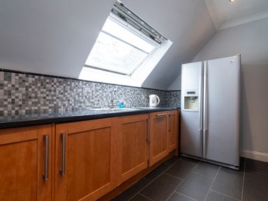 A kitchen with wooden cabinets black countertop a stainless steel refrigerator and a skylight window at The Gables Penthouse in Bournemouth