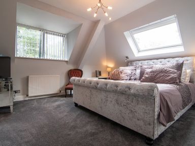 A bedroom with a large bed multiple pillows a red chair a modern light fixture and windows at The Gables Penthouse in Bournemouth