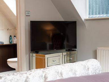 A television on a mirrored cabinet next to a bathroom with a toilet and toiletries visible at The Gables Penthouse in Bournemouth