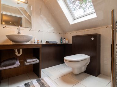 A bathroom with a wall-mounted toilet sink towels and toiletries under a skylight window at The Gables Penthouse in Bournemouth