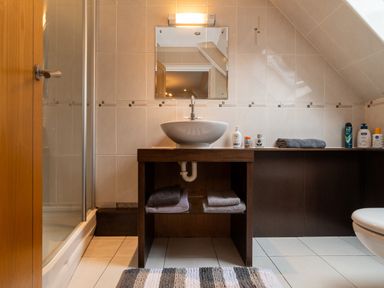 A bathroom with a sink on a wooden vanity mirror above a wooden vanity with towels and toiletries at The Gables Penthouse in Bournemouth
