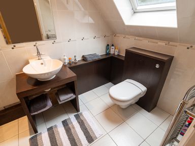 A bathroom with a sink on a wooden vanity a wall-mounted toilet toiletries on a built-in shelf and a window at The Gables Penthouse in Bournemouth