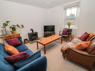 A living room with sofas a wooden coffee table a television and a window with flowers at Tyne View Cottage in Bellingham