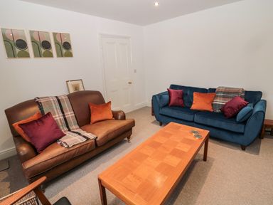 A living room with two sofas a wooden coffee table and abstract paintings on the wall at Tyne View Cottage in Bellingham