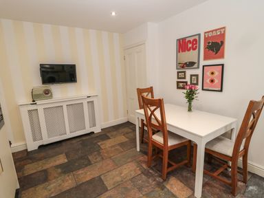 A dining area with wooden chairs around a white table with flowers and wall art at Tyne View Cottage in Bellingham