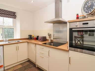A kitchen with cream cabinets wooden countertops a black electric stove a stainless steel oven and hood and a window with patterned blind at Tyne View Cottage in Bellingham