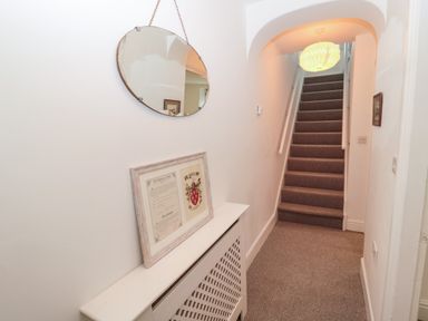 A hallway with carpeted stairs and a round mirror hanging above a radiator cover at Tyne View Cottage in Bellingham