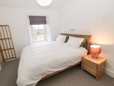 A bedroom with a bed a wooden headboard a bedside table with a lamp and a window with a patterned blind at Tyne View Cottage in Bellingham